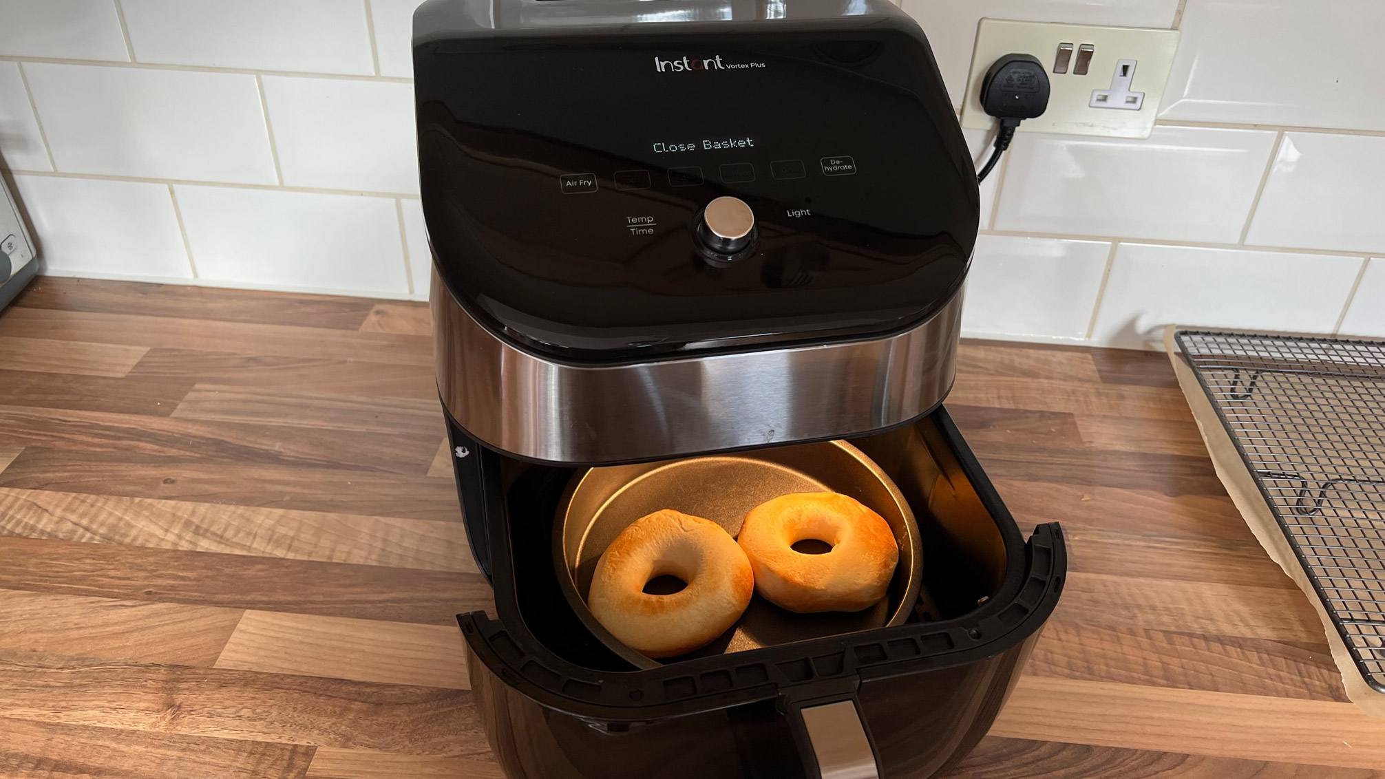 Two donuts in a metal tin in the basket of an air fryer, partway through cooking